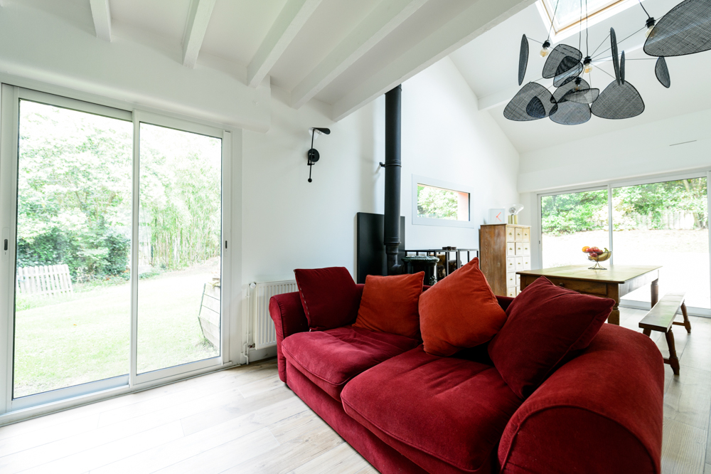 08-salon-exterieur-interieur-verdure-canape-rouge-velours-suspension-cannage-designer-poele-bois-convivial-chaleureux-lumineux